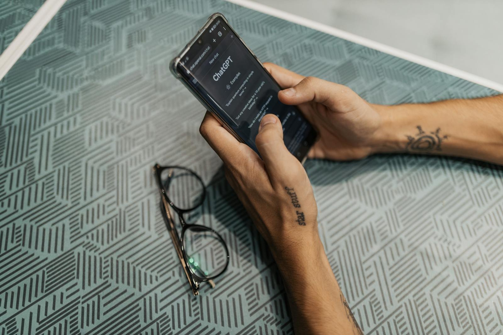 Photo by Matheus Bertelli - copyfind.net Close-up of a person holding a smartphone showing the ChatGPT app next to eyeglasses.